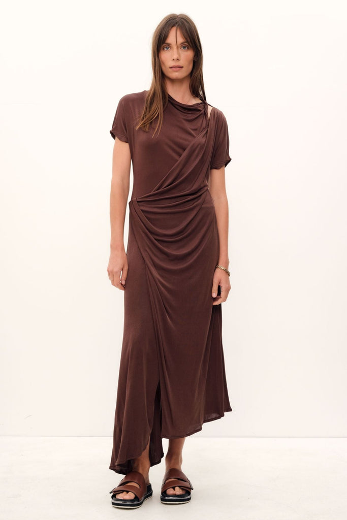 The Aphrodite Draped Dress, exquisitely crafted in silk viscose jersey of a coco hue, boasts a relaxed silhouette with an asymmetric hem and sleeves, a cinched waistline that gracefully drapes, a delicate stretch fabric, and a midi length with a sublime twist detail across the neck and shoulder.